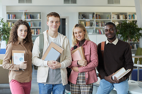 Portrait of multi-ethnic group of students looking at camera and smiling while standing in college library