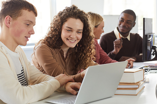 Portrait of smiling young woman looking at laptop screen while studying with group of students in college library