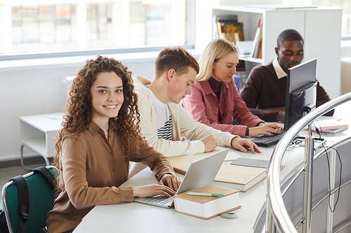 Portrait of smiling young woman looking at camera and smiling while studying with group of students in college library