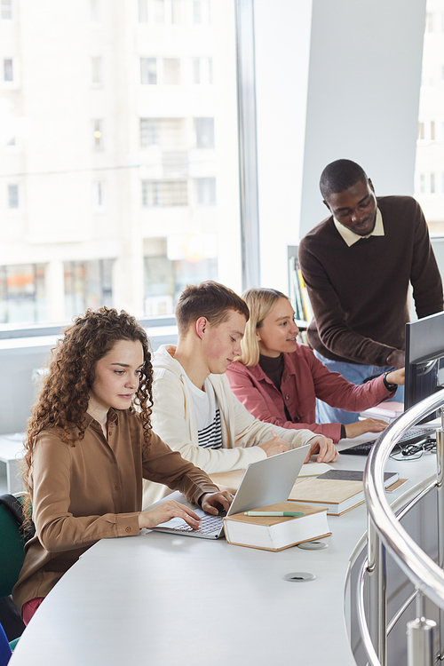 Vertical side view portrait of multi-ethnic group of students using laptops while studying in college