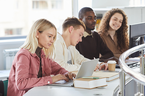 Side view portrait of group of students using laptops while studying in college, blonde girl typing in foreground, copy space