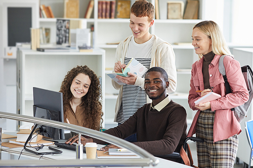 Multi-ethnic group of students using telecommunication equipment while studying in college library, focus on African-American man smiling at camera, copy space