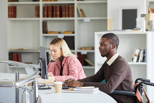 Side view portrait of young African-American man using computer while studying in college library, copy space