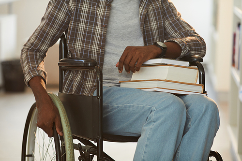 Cropped portrait of unrecognizable African-American man using wheelchair in school in library with focus on books, copy space