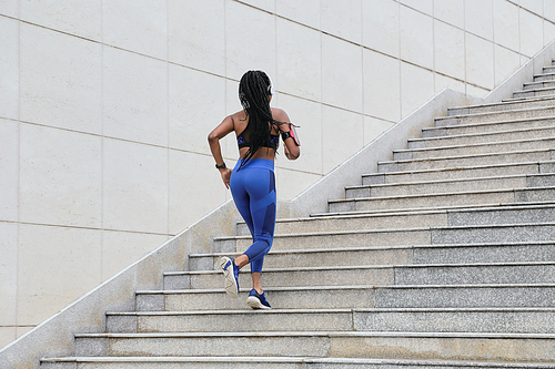 Fit young woman in blue leggings running up the stairs, view from the back