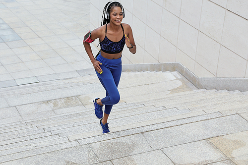 Happy young sportswoman jogging in the morning and listening to music in headphones