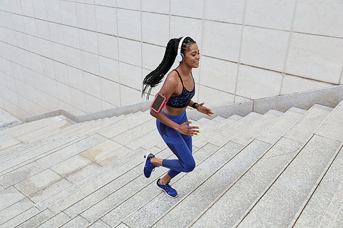 Young fit sportswoman enjoying good music in her heaphones when jogging in the city