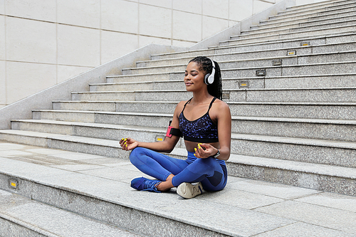 Pretty young African-American sportswoman meditating and listening to relaxing music in headphones