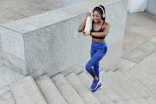 Sportswoman wiping sweat with towel and checking ammount of calories she burned during morning run via app in smartwatch