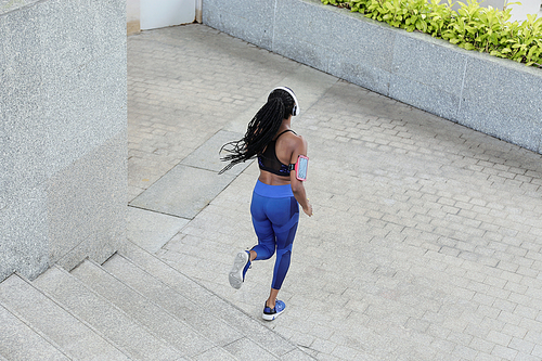 Beautiful fit young woman with dreadlocks running in the street, view from the back