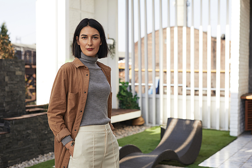 Portrait of confident modern woman wearing minimal casual clothes while standing on outdoor terrace and looking at camera, copy space