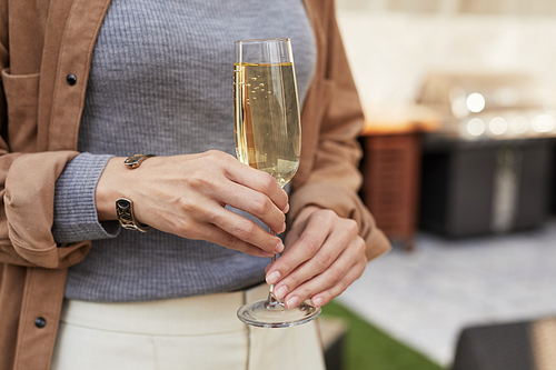 Close up of elegant woman holding champagne flute while standing at outdoor terrace during party, copy space
