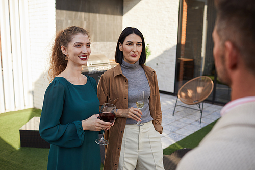 Waist up portrait of contemporary adult women chatting with friends and smiling while standing at outdoor terrace during party, copy space