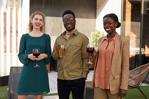Waist up portrait of contemporary African-American people looking at camera while enjoying wine standing at outdoor terrace during party