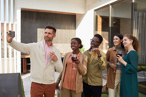 Waist up portrait of multi-ethnic group of friends taking selfie photo while enjoying party standing at outdoor terrace