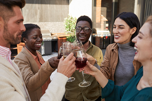 Portrait of multi-ethnic group of friends clinking glasses while enjoying wine during outdoor party at terrace