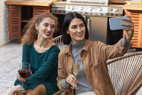 Portrait of two elegant women taking selfie photo and smiling at camera while enjoying outdoor party at terrace, copy space