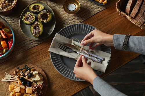 High angle close up of female hands tying napkins and silverware while decorating dinner table in autumn, copy space