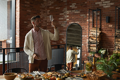 Portrait of elegant mature man inspecting glasses while serving dinner table for Thanksgiving party at home, copy space