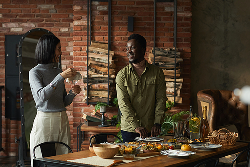 Portrait of contemporary mixed-race couple serving dinner table for Thanksgiving party at home, copy space