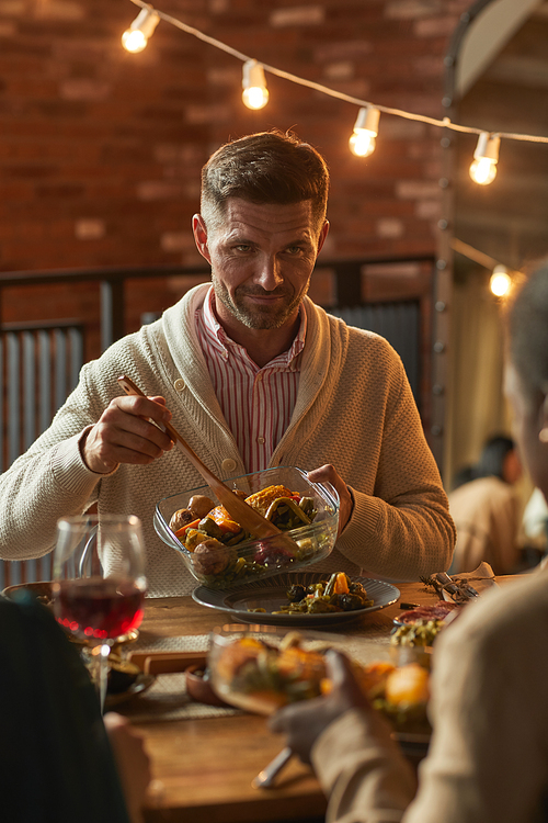 Vertical portrait of handsome mature man serving food while hosting dinner party with friends and family