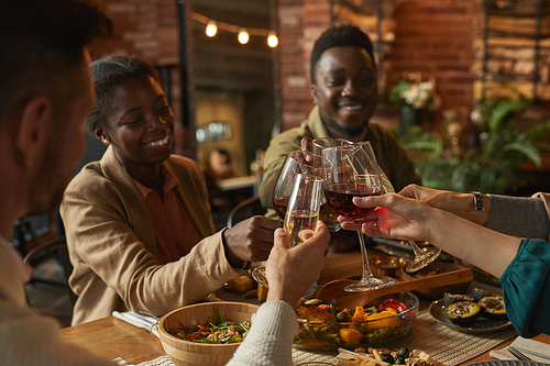 Portrait of happy African-American couple clinking glasses while enjoying dinner party with friends and family in cozy interior