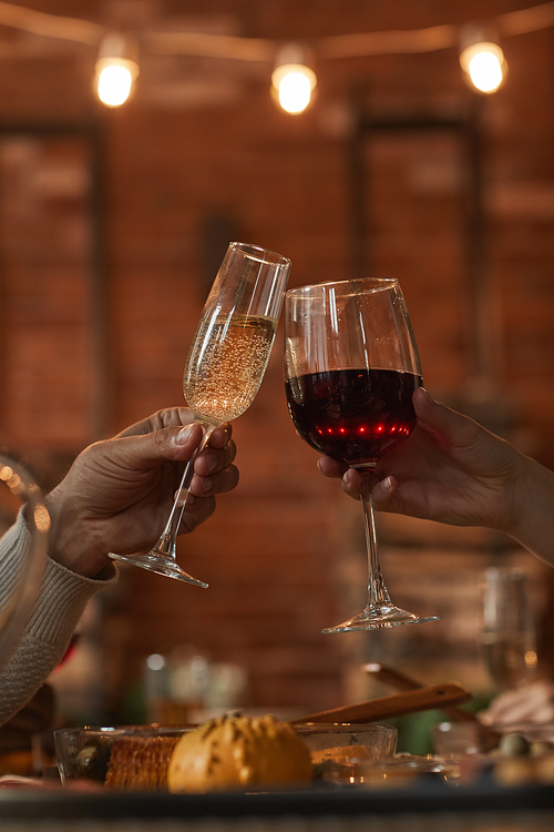 Vertical close up of unrecognizable loving couple clinking glasses while enjoying dinner date in romantic ambience