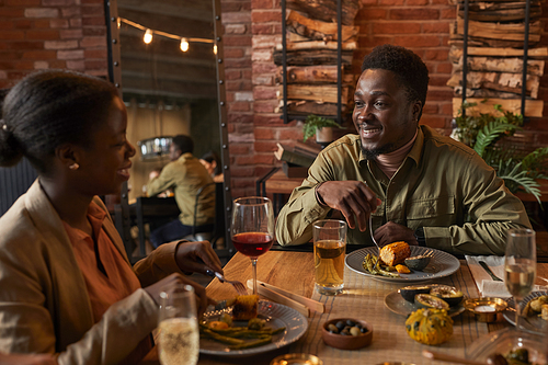 Portrait of young African-American man smiling at girlfried while enjoying dinner party outdoors