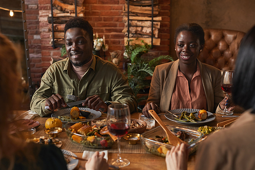 Portrait of smiling African-American couple enjoying dinner party with friends in cozy lighting