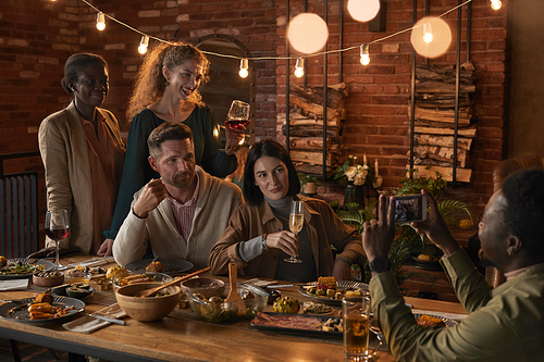 Multi-ethnic group of cheerful adult people taking photo while enjoying party with outdoor lighting