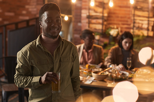 Waist up portrait of smiling African-American man holding champagne glass and looking at camera while enjoying party outdoors, copy space