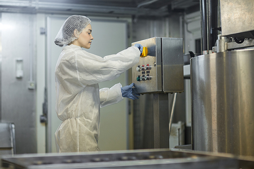 Side view portrait of young female worker operating machine units at clean food production factory, copy space