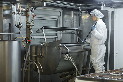 Wide angle view female worker using mixing machine at clean food production factory, copy space