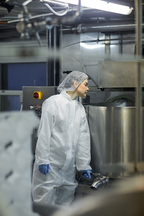 Vertical portrait of young female worker using machines at clean food production factory, copy space