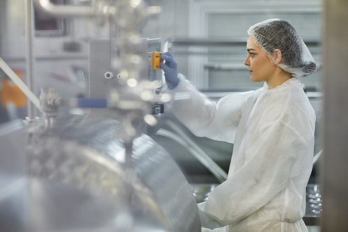 Side view portrait of female worker pushing button while operating machine units at clean food production factory, copy space