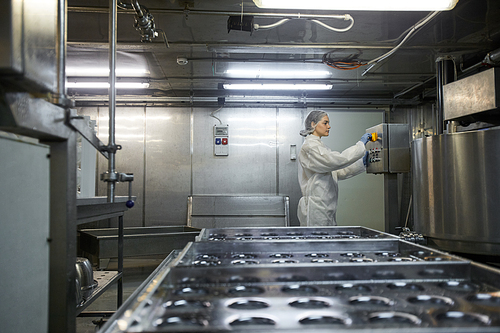 Wide angle side view at young female worker operating machine units at clean food production factory, copy space