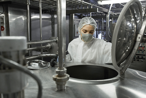 Portrait of young female worker wearing mask while operating mixing machine at clean food production factory, copy space