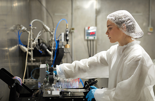 Side view portrait of young female worker operating equipment while working at factory, copy space