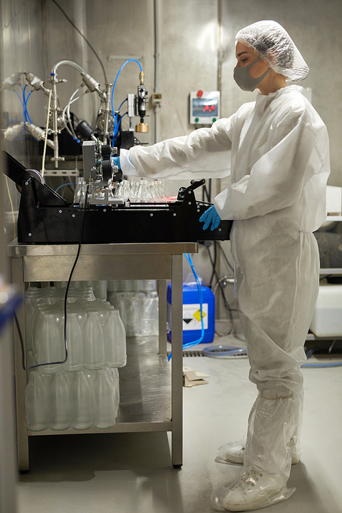 Full length side view of young female worker operating equipment while working at food factory