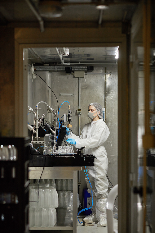 Vertical long shot at young female worker wearing mask and operating equipment while working at food factory, copy space