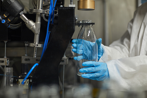 Close up of unrecognizable female worker disinfecting bottles while working at food factory, copy space