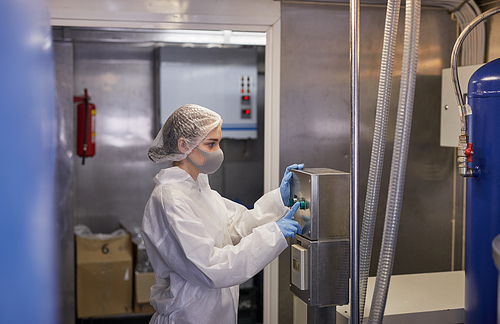 Side view portrait of young female worker pushing buttons at control panel while operating machines at food factory, copy space