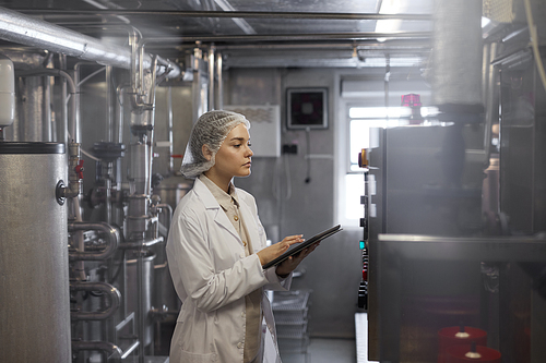 Side view portrait of female worker holding digital tablet during quality control inspection at food factory workshop, copy space