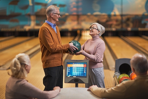 Portrait of happy senior couple playing bowling together with group of friends at entertainment center, copy space