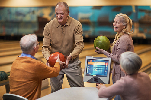 Group of senior people playing bowling together while enjoying active entertainment at bowling alley, copy space