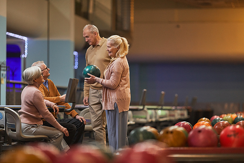 Wide angle side view at group of senior people playing bowling together while enjoying active entertainment at bowling alley, copy space