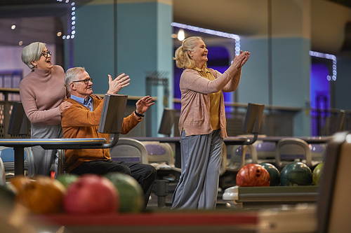 Side view at group of senior people playing bowling together while enjoying active entertainment at bowling alley, copy space