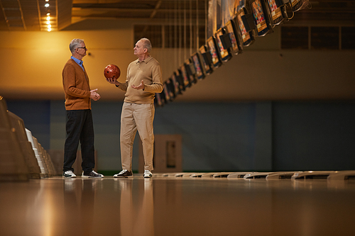 Wide angle side view at two senior friends playing bowling together while enjoying active entertainment at bowling alley, copy space