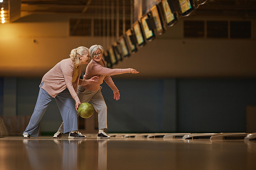 Wide angle side view at two senior women playing bowling together while enjoying active entertainment at bowling alley, copy space