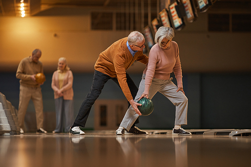 Wide angle side view at modern senior couple playing bowling together while enjoying active entertainment at bowling alley, copy space